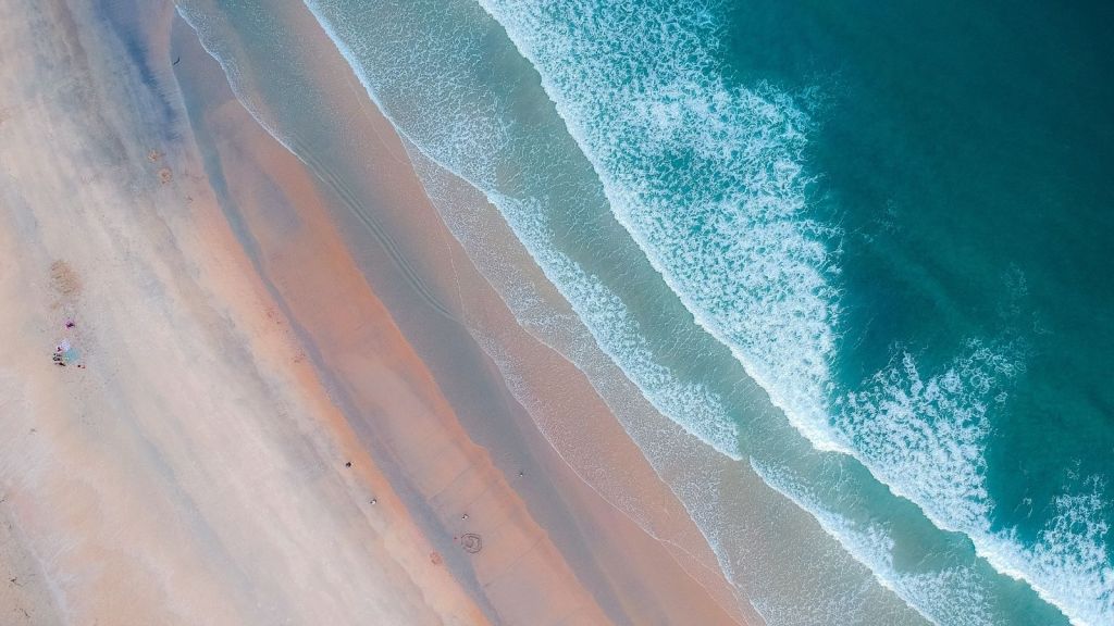 Soft background image of a beach with waves rippling in from the top right