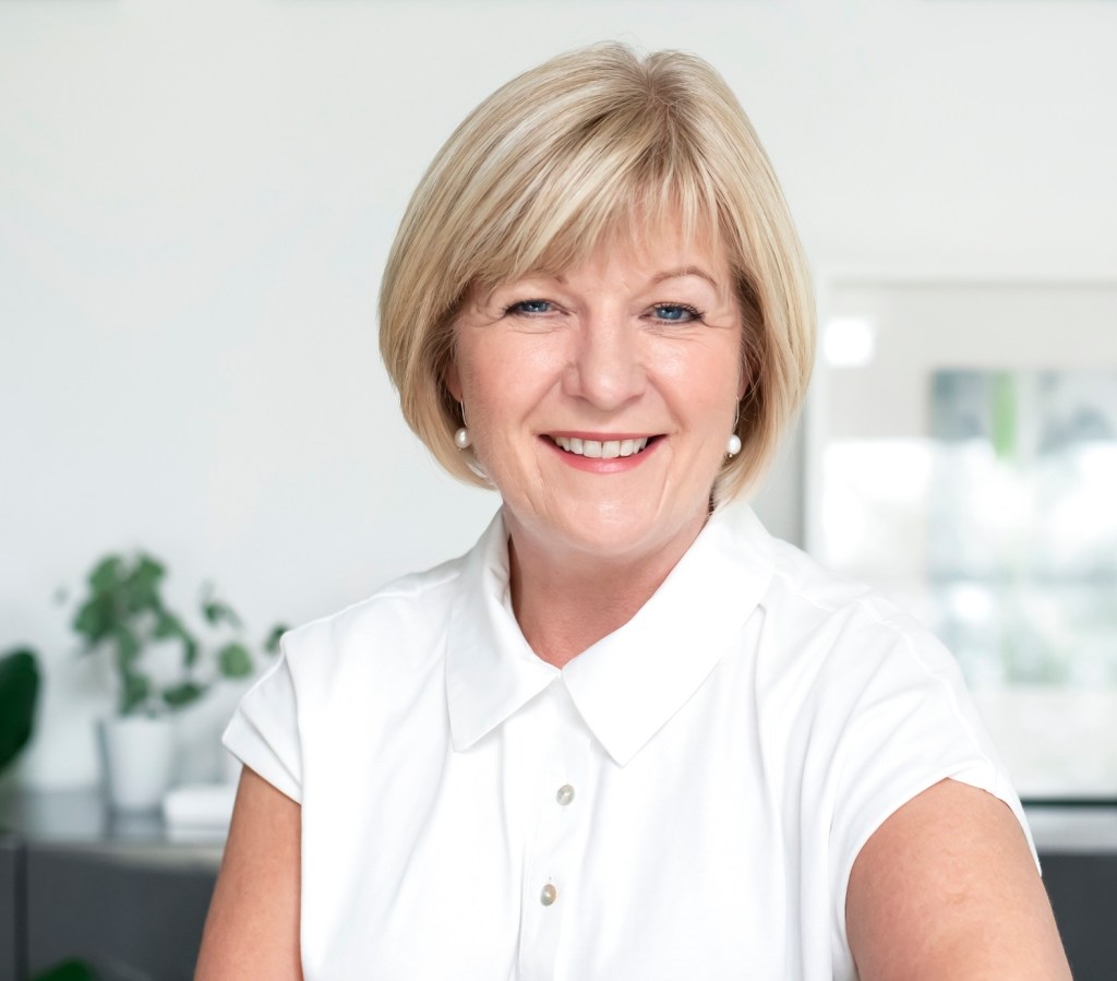 Christine wears a white, short-sleeved top and is smiling